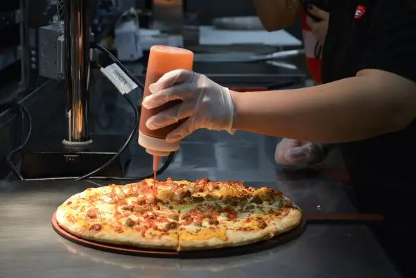 Store associate putting toppings on a taco pizza